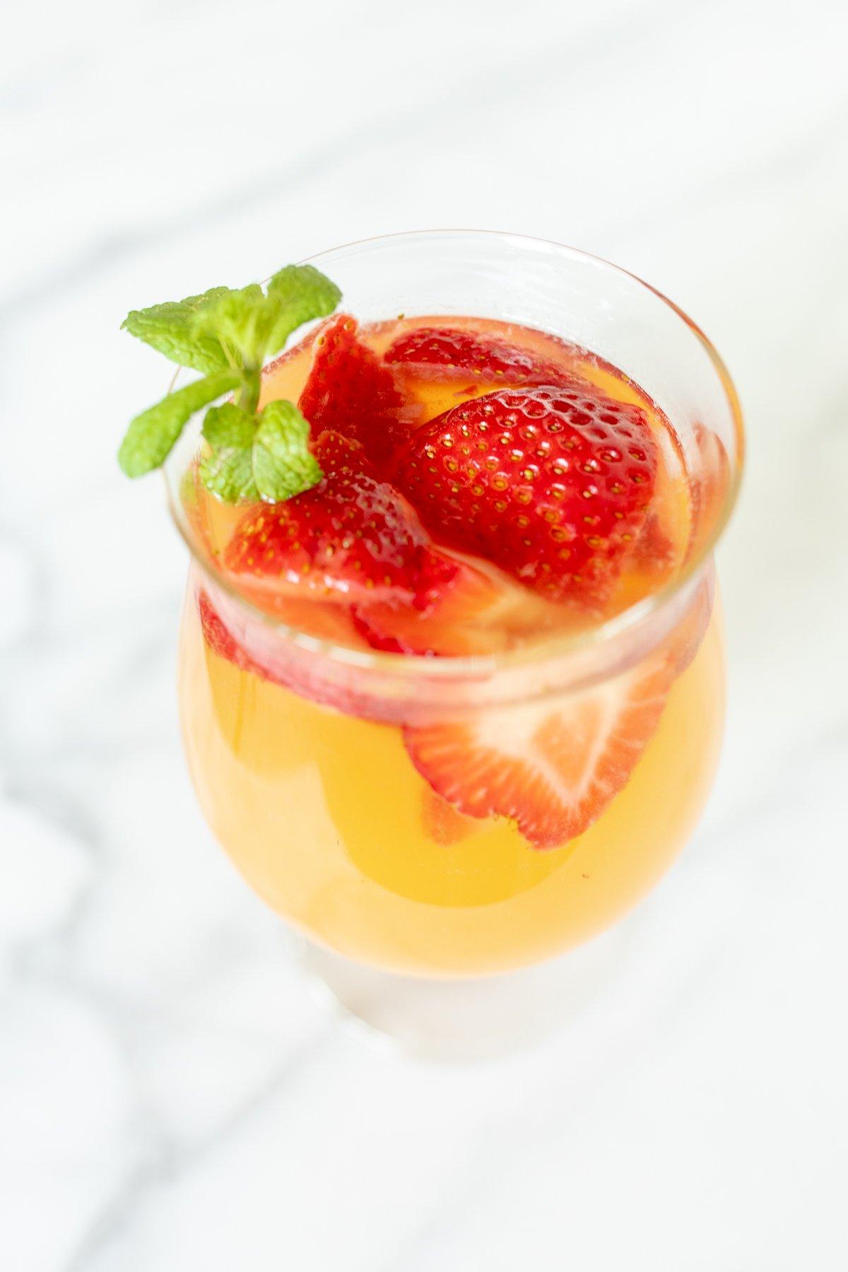 Ein Glas Moscato Sangria, garniert mit Erdbeeren, Pfirsichen und Minze.
