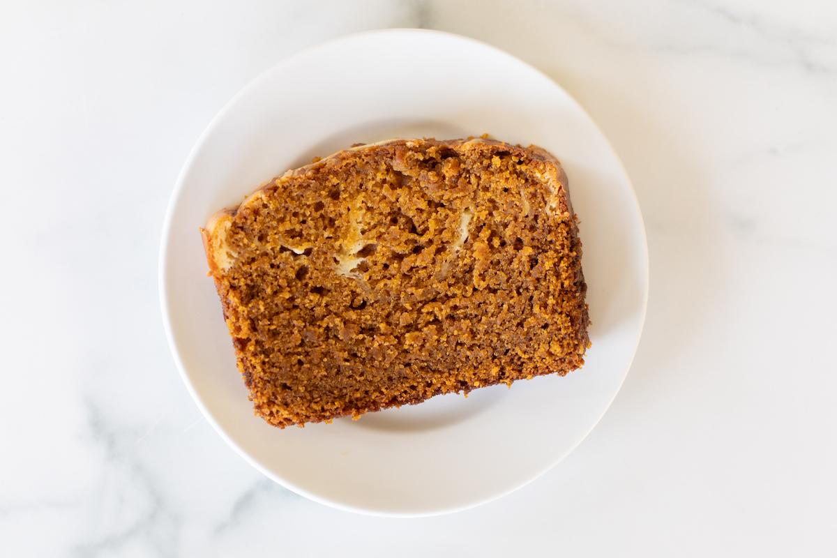Eine perfekt geschnittene Scheibe Kürbis-Käsekuchen-Brot mit deutlich sichtbarer cremiger Füllung auf einem weißen Teller.