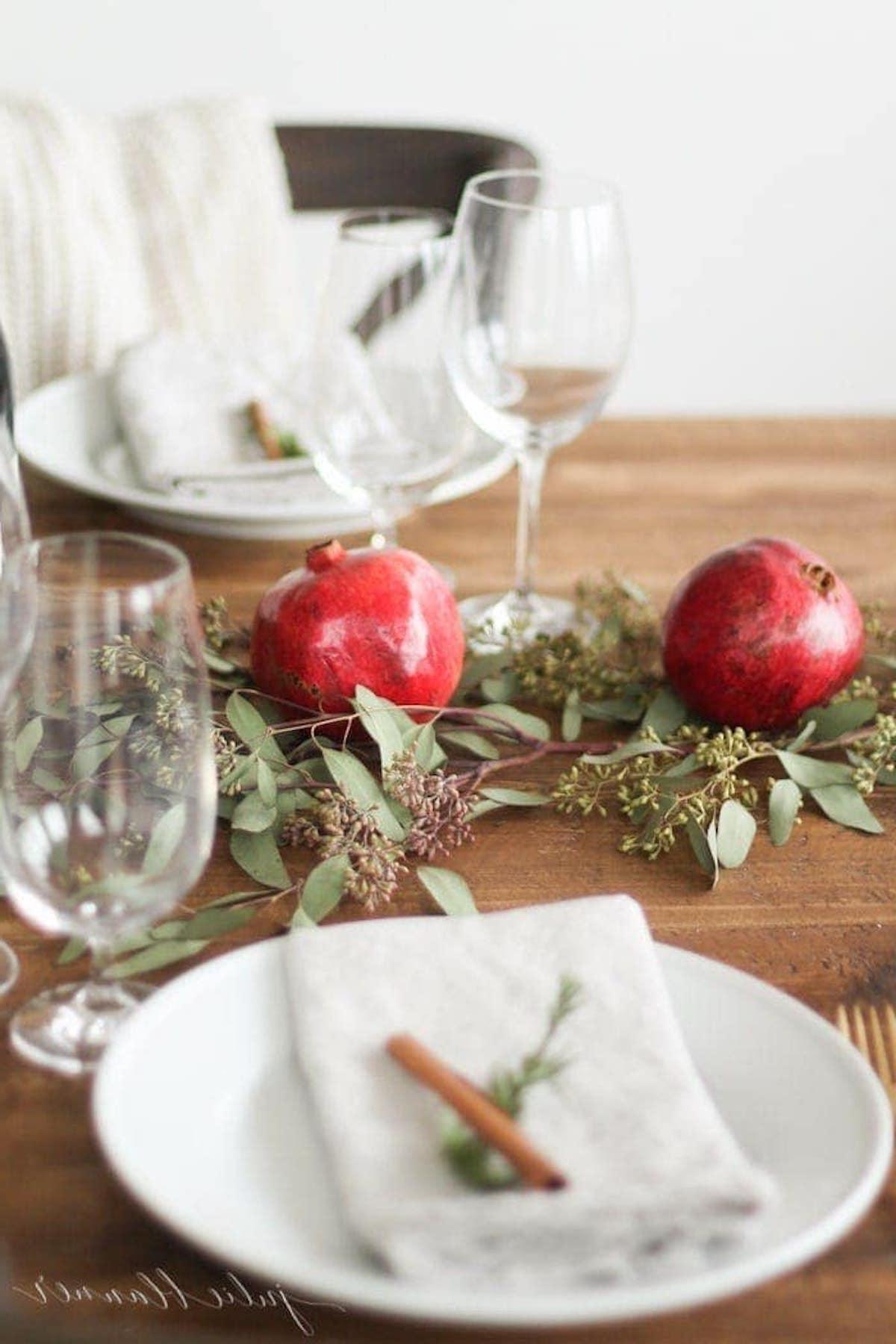 Ein gedeckter Tisch mit einem Weihnachts-Kerzen-Mittelstück, geschmückt mit Granatäpfeln und Eukalyptusblättern.