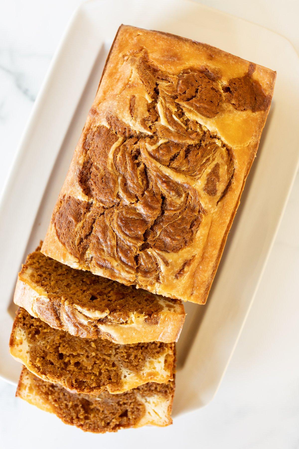 Ein appetitlicher Laib Kürbis-Käsekuchen-Brot auf einer weißen Platte, der eine perfekte Backfarbe und Textur aufweist.