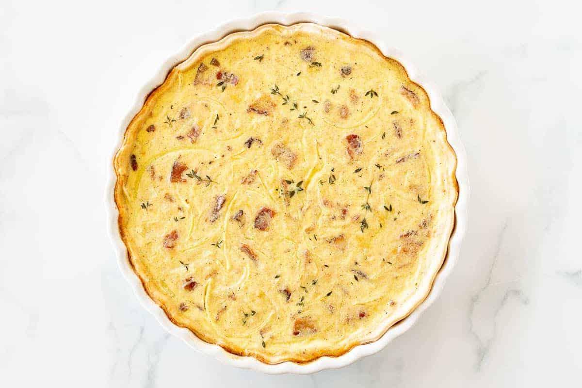Muttertags-Brunch-Ideen 23 Eine ganze Quiche in einer weißen Kuchenform auf einer weißen Marmoroberfläche.