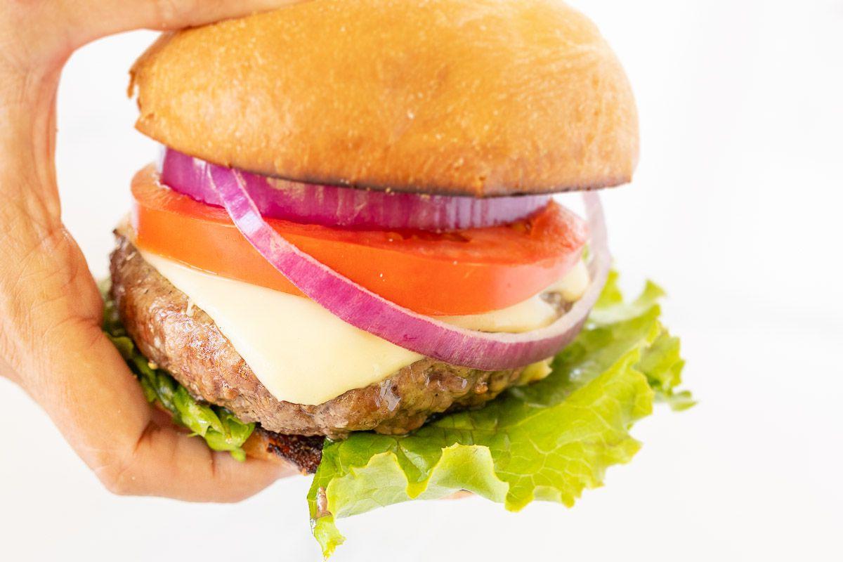 Warum man Burgerbrötchen rösten sollte 4 Ein Burger mit vielen Belägen und einem getoasteten Burger Bun, in der Hand gehalten