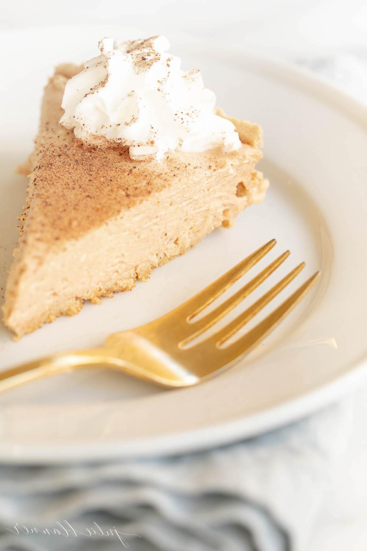 Einfaches Kürbis-Käsekuchen-Rezept ohne Backen 4 Kürbis-Käsekuchen mit Schlagsahne gekrönt auf einem weißen Teller, daneben eine goldene Gabel.