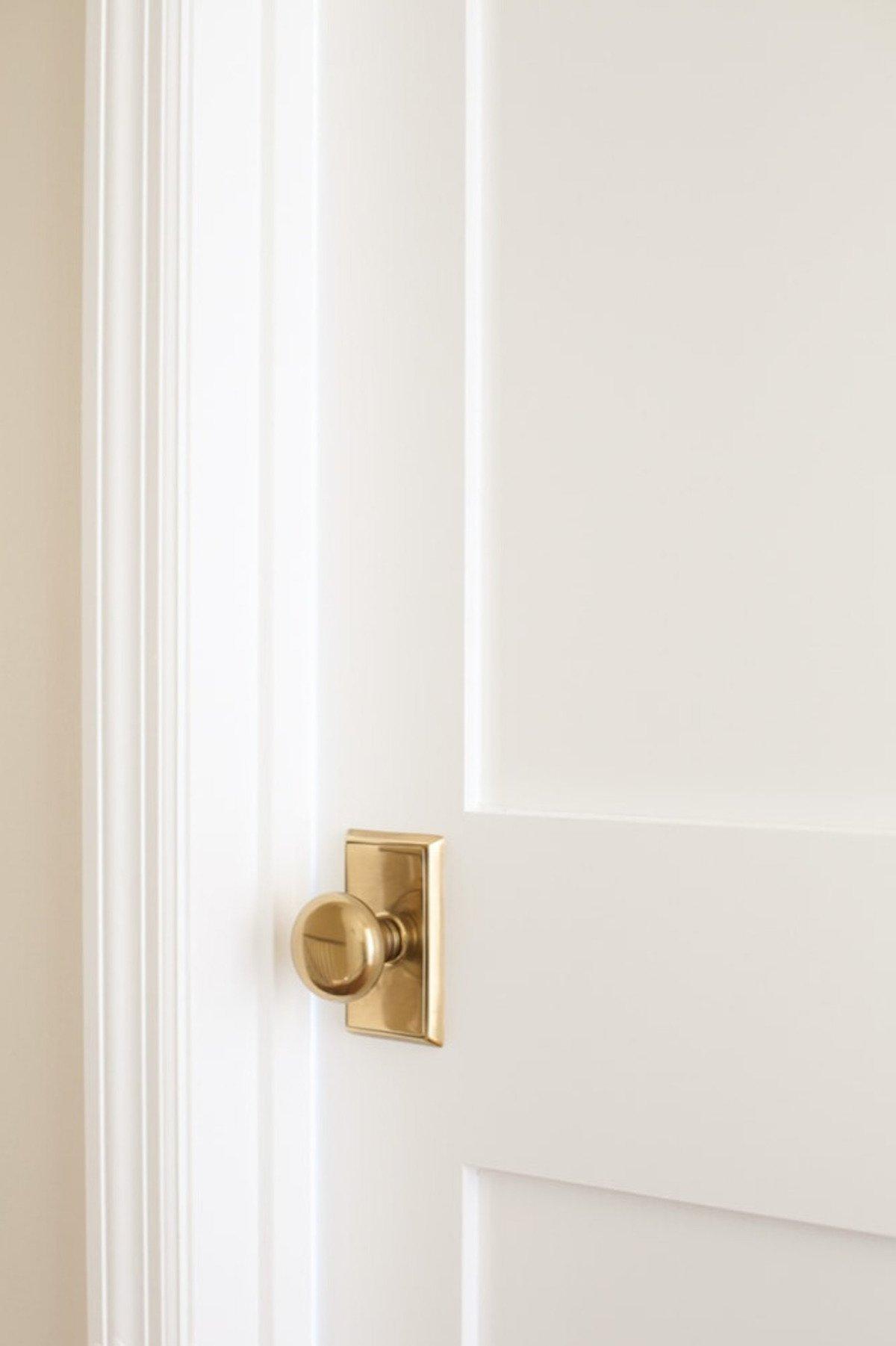 Innentüren streichen 4 Eine teilweise geöffnete weiße Tür mit Messingknauf und Zierleisten, frisch gestrichen für ein Interieur-Makeover.