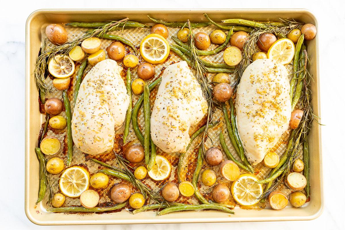 Rosmarinhähnchen 4 Drei Rosmarin-Hähnchenbrüste mit Zitronenscheiben, grünen Bohnen und Kartoffeln auf einem Backblech, gewürzt mit Gewürzen.