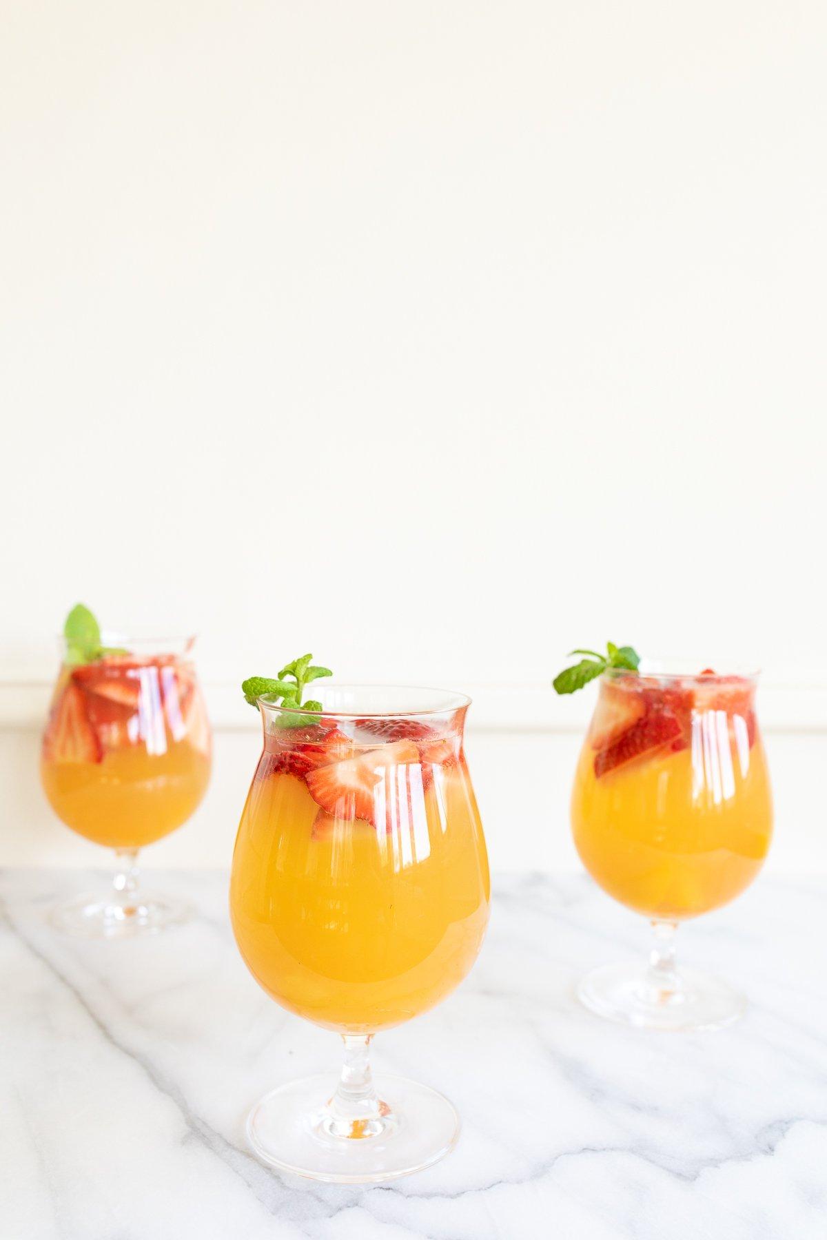Drei Gläser Moscato Sangria, garniert mit Erdbeeren, Pfirsichen und Minze.