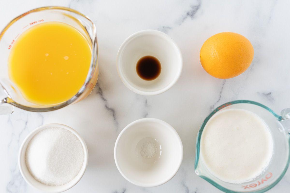 Orangen-Sorbet 4 Schlagsahne, Vanilleextrakt und Orangensaft, bereit für die Zubereitung, auf einer Marmoroberfläche