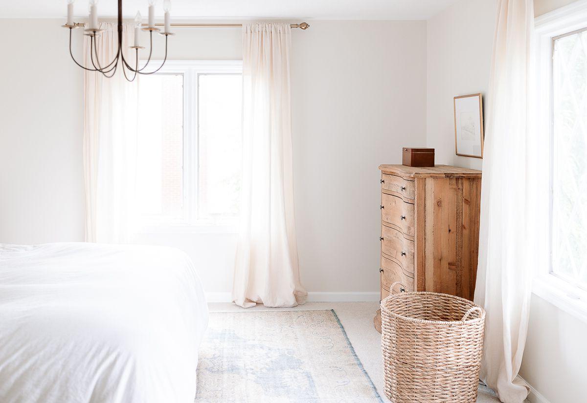 Teppiche auf Teppichboden schichten? 5 Ein sanftblauer antiker Teppich auf Teppichboden in einem weißen Schlafzimmer, Holzkommode in der linken Ecke.