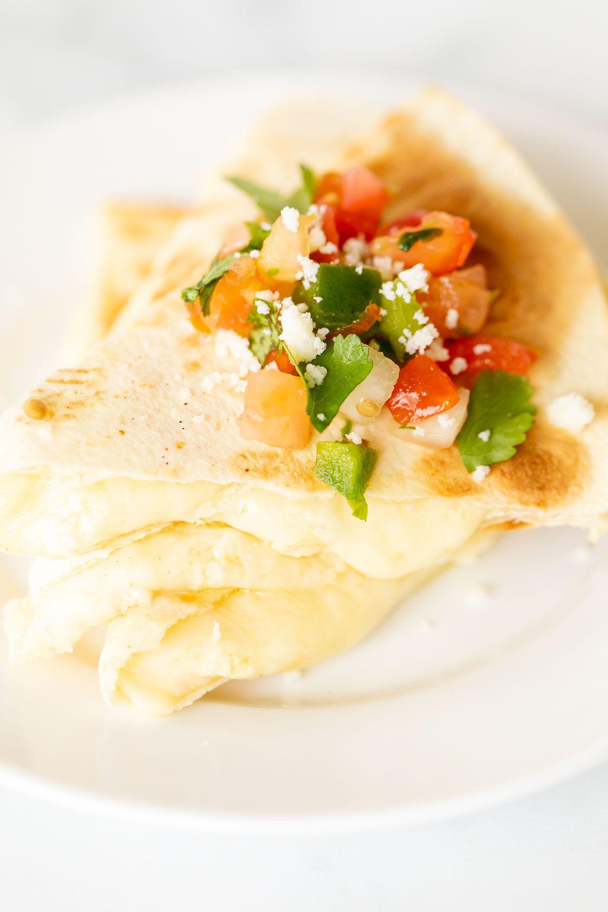 Käsequesadillas 5 In Scheiben geschnittene und gestapelte Käse-Quesadilla auf einem weißen Teller, mit Pico de Gallo belegt