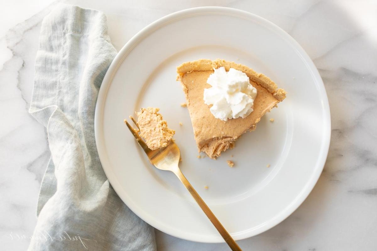 Einfaches Kürbis-Käsekuchen-Rezept ohne Backen 5 Kürbis-Käsekuchen mit Schlagsahne gekrönt auf einem weißen Teller, daneben eine goldene Gabel.