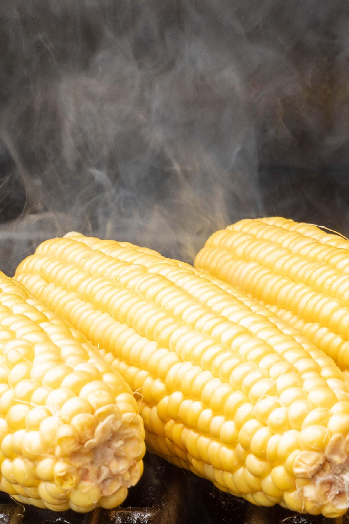 Gegrillter Maiskolben 5 Drei Maiskolben vom Grill mit aufsteigendem Dampf im Hintergrund.