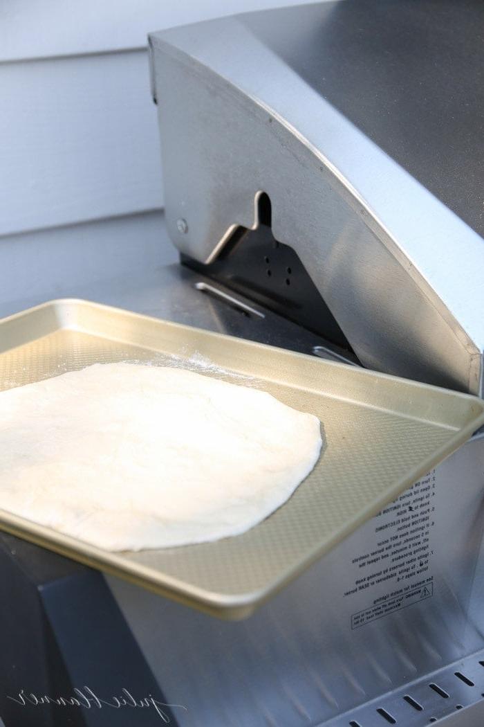 Pizzateig auf einem goldenen Backblech in der Nähe eines Grills