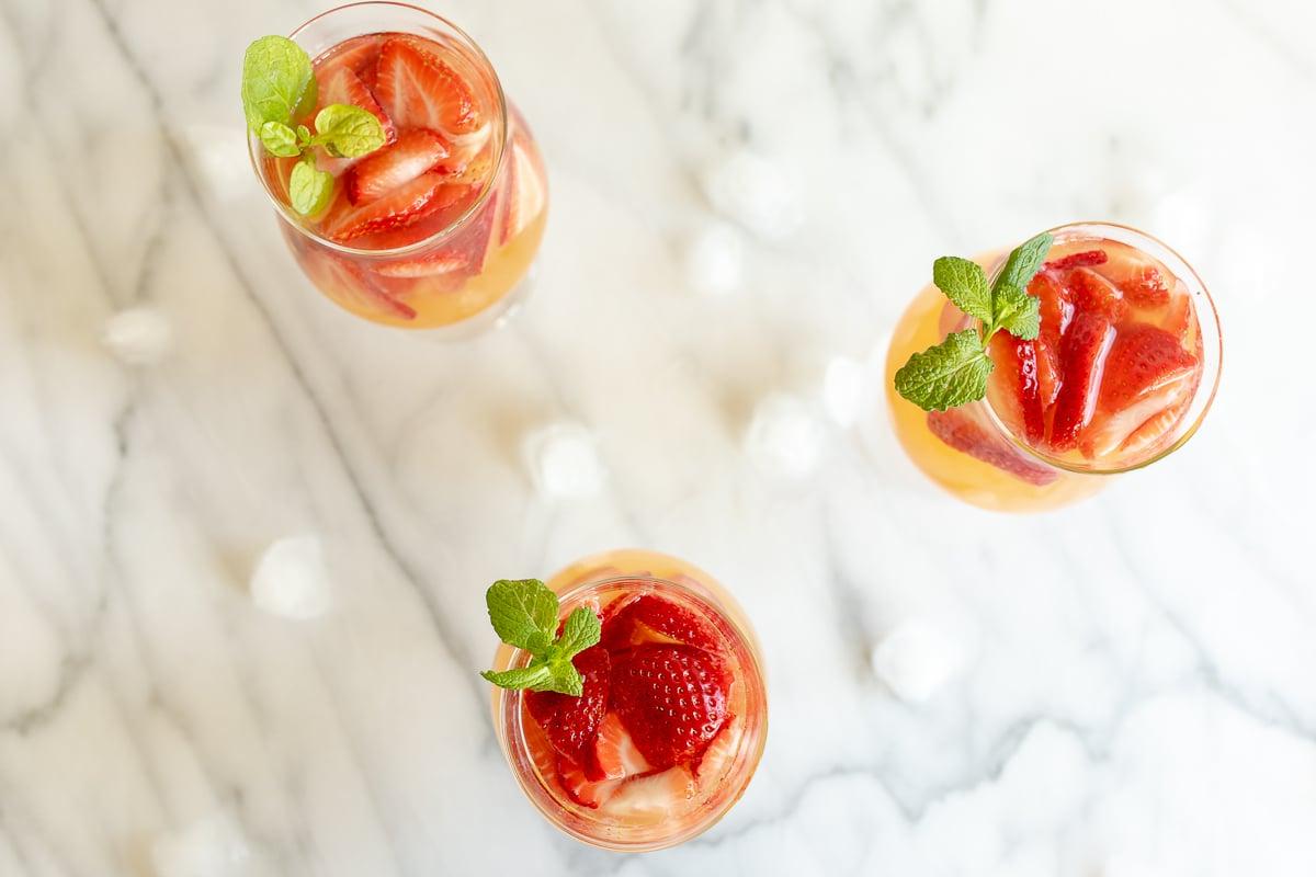 Drei Gläser Moscato Sangria, garniert mit Erdbeeren, Pfirsichen und Minze.