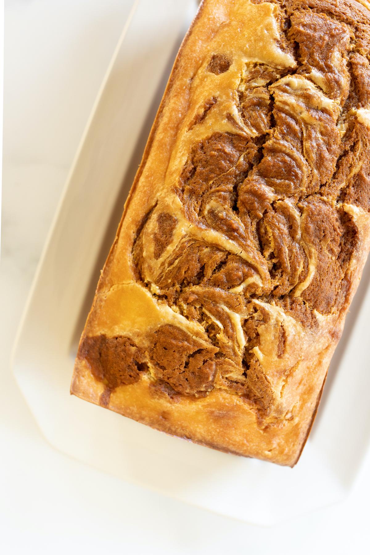Ein frisch gebackener Laib Kürbis-Käsekuchen-Brot auf einer weißen Platte, dessen goldbraune Kruste verführerisch glänzt.