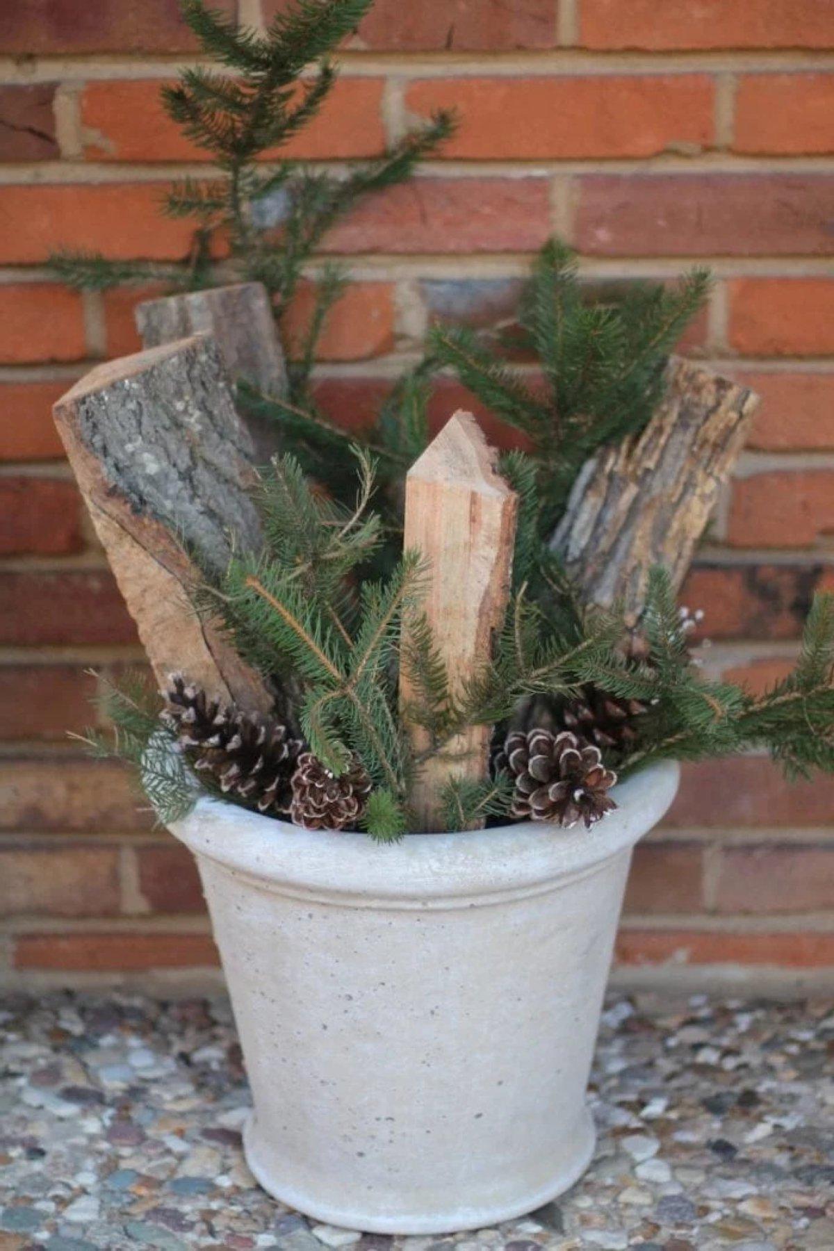 Ein Winterkübel für die Veranda mit geschnittenem Brennholz, immergrünen Pflanzen und Kiefernzapfen.