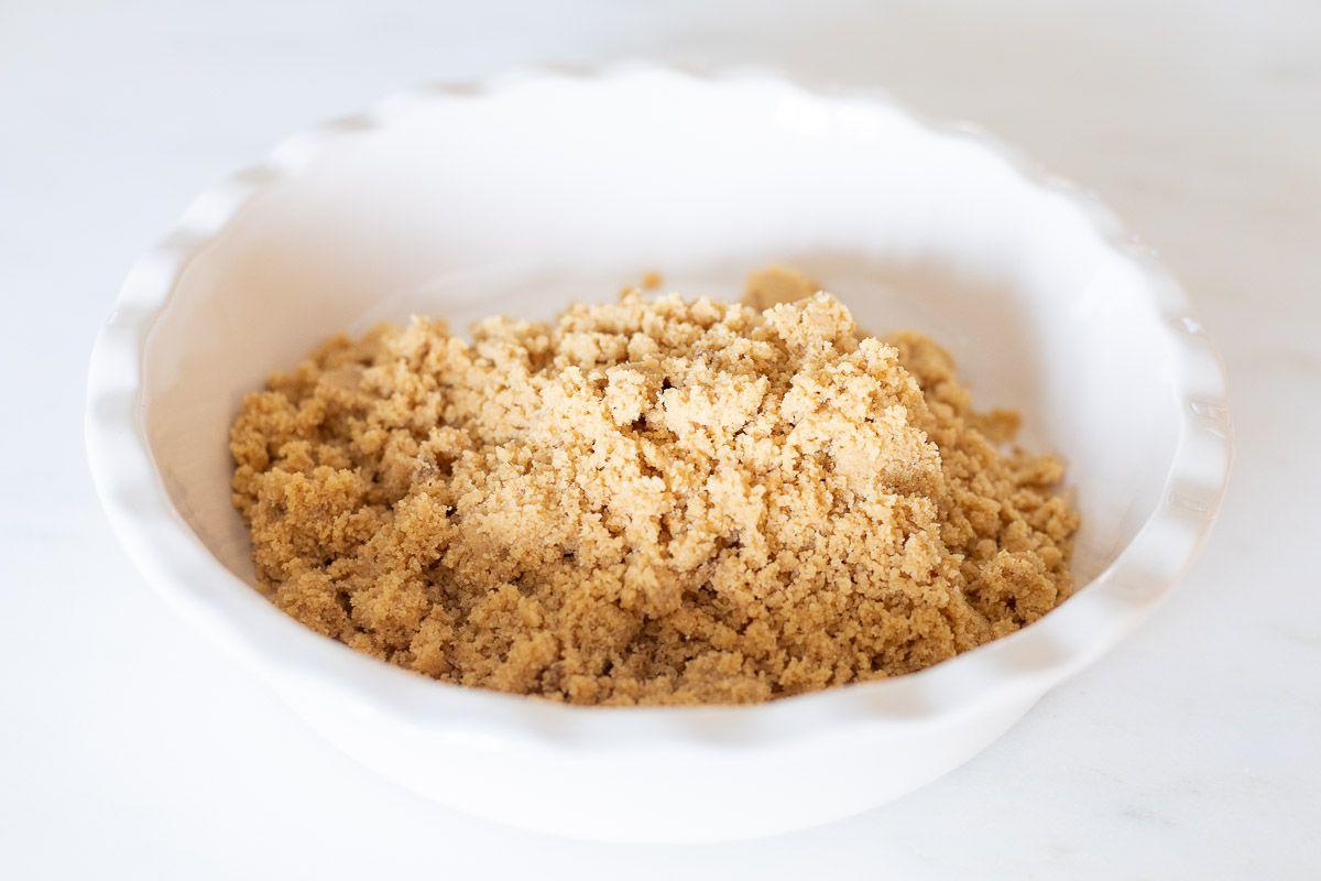 Zutaten für einen No-Bake Shortbread-Kuchenboden in einer weißen, geriffelten Keramik-Kuchenform