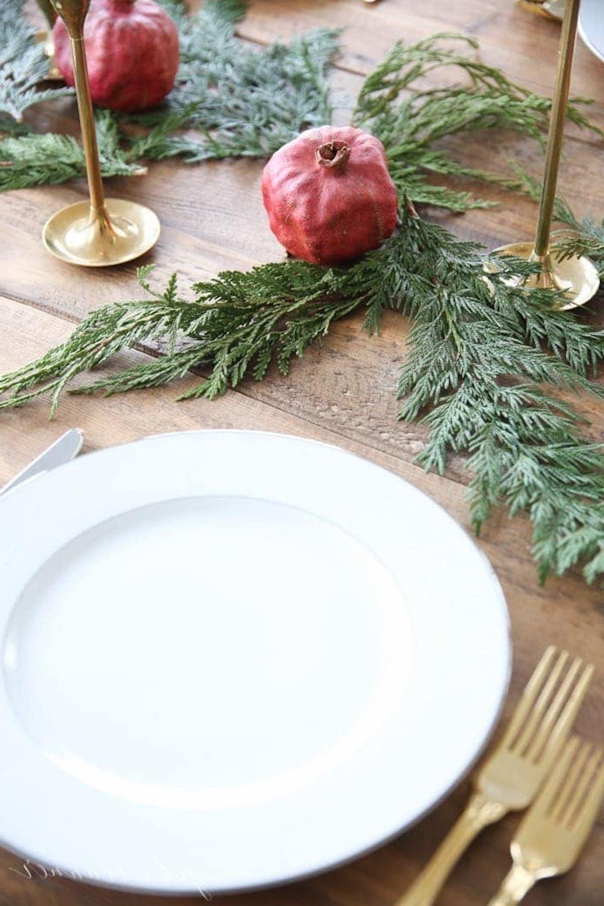 Ein festlich gedeckter Weihnachtstisch mit einem Weihnachts-Kerzen-Mittelstück, geschmückt mit Granatäpfeln und Grünzeug.