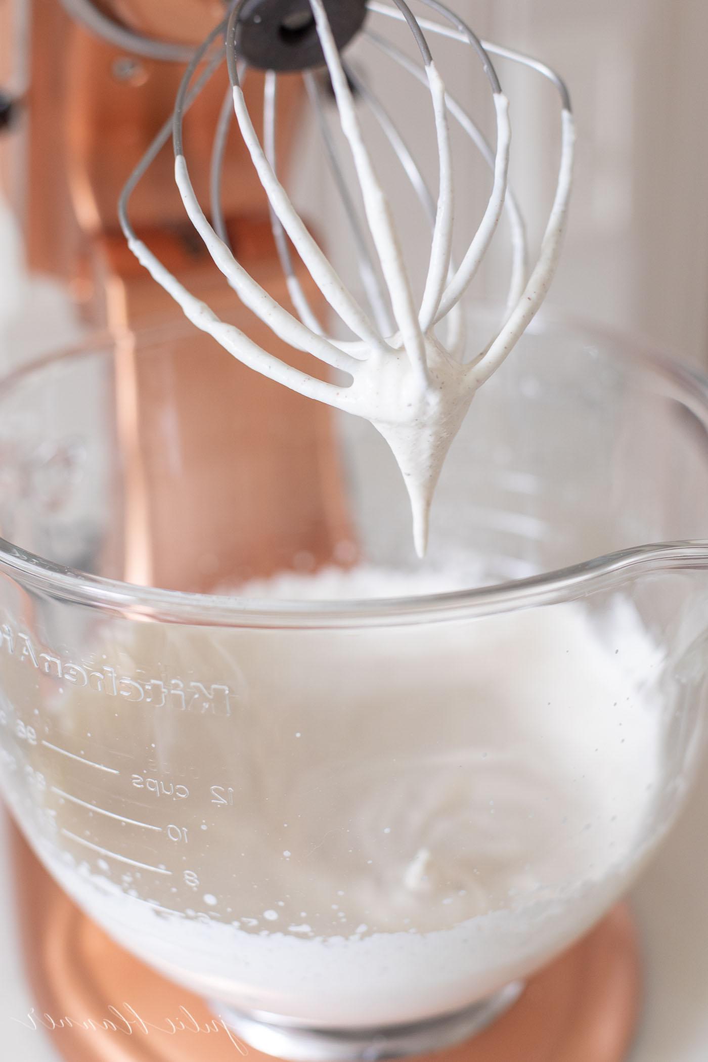 Eierpunsch-Schlagsahne in der Glasschüssel eines kupferfarbenen Standmixers während des Mixvorgangs, der Eierpunsch wird gerade eingerührt.