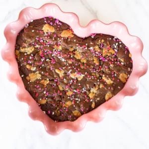 Bachforelle 6 Herzförmiger Brookie mit rosa und weißen Streuseln in einer rosa gewellten Schale auf einer Marmoroberfläche.