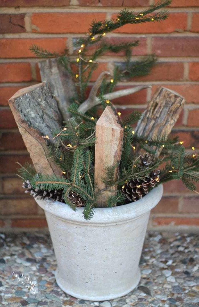 Weihnachtliche Türdekorationen 6 Einfaches Pflanzgefäß gefüllt mit immergrünen Pflanzen, Holzscheiten und Tannenzapfen für die Weihnachtsdekoration