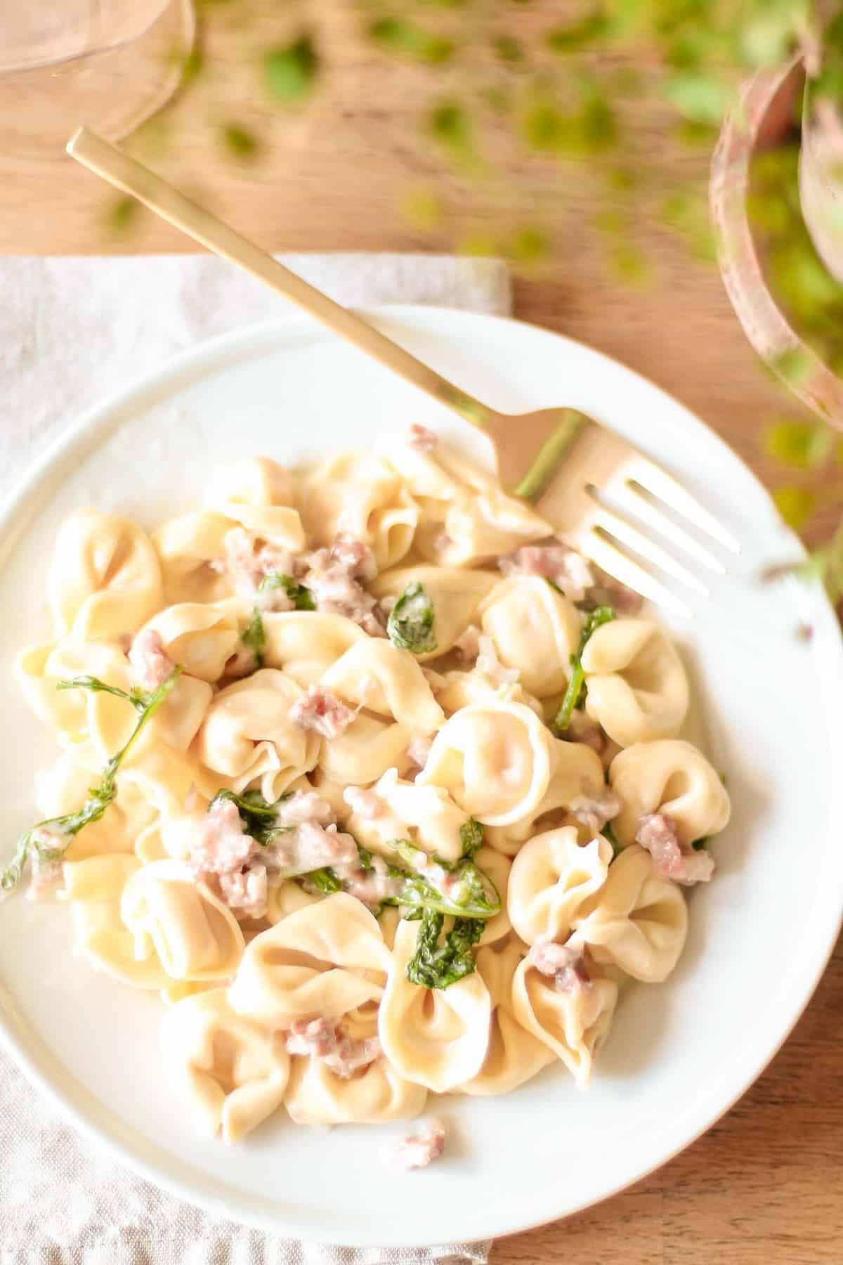 Tortellacci mit Prosciutto, Rucola und Trüffelöl auf weißem Teller mit goldener Gabel