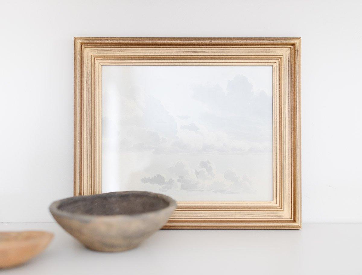 **Freie Kunstquellen** 6 Ein gerahmter Druck von Wolken und einer Schale auf einem Tisch, aus der Public Domain Kunstsammlung von Studio McGee stammend.