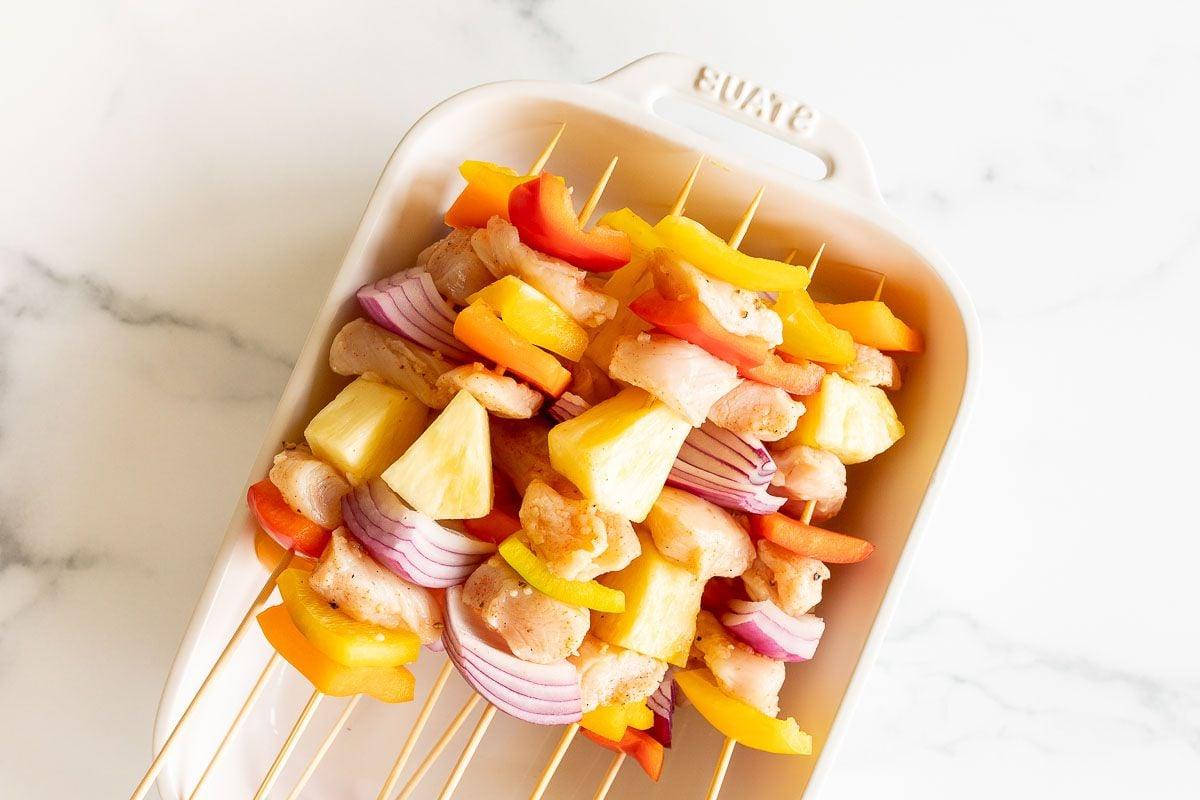 **Einfache Hähnchenspieße** 7 Ungekochte Hähnchenspieße in einer weißen Auflaufform vor dem Grillen