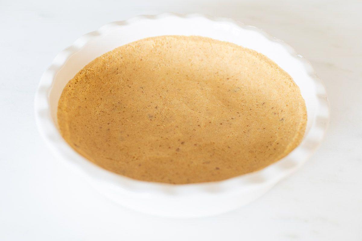 Ein Shortbread-Kuchenboden, in eine weiße, geriffelte Keramik-Kuchenform auf einer Marmoroberfläche gepresst