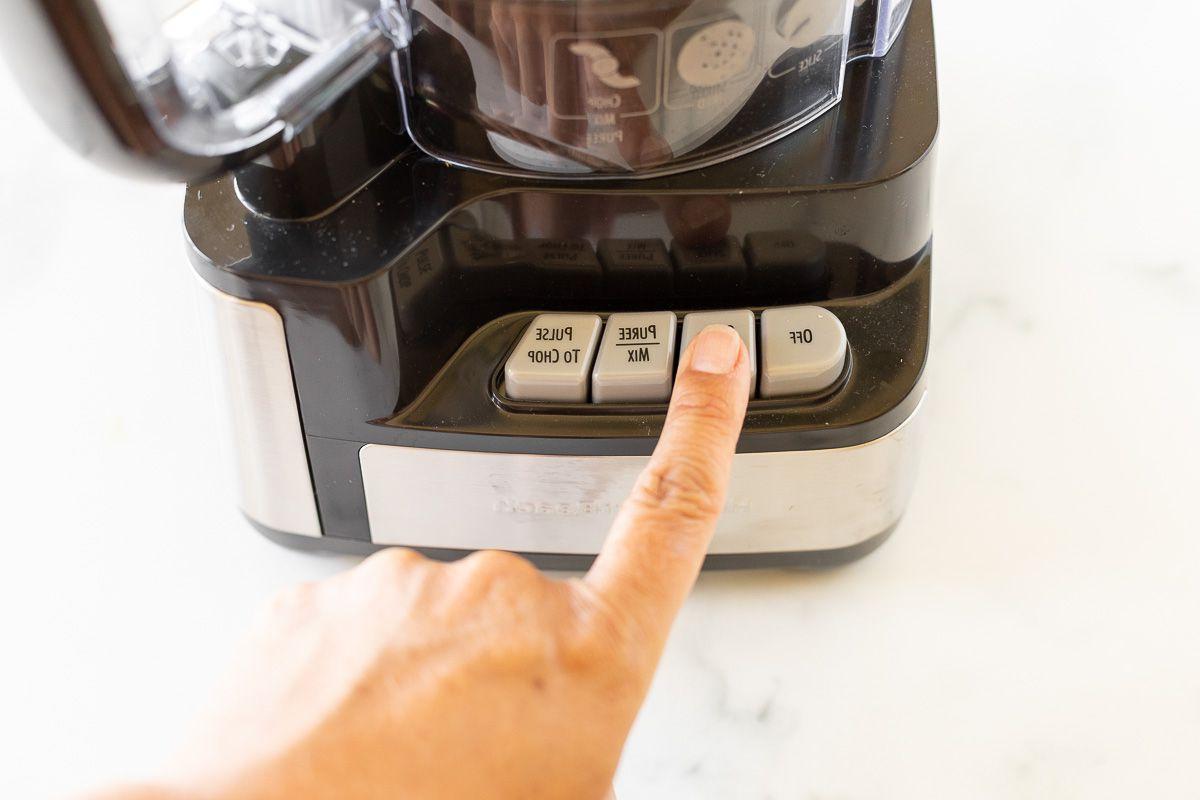 Ein Finger drückt einen Knopf an einem Food Processor.
