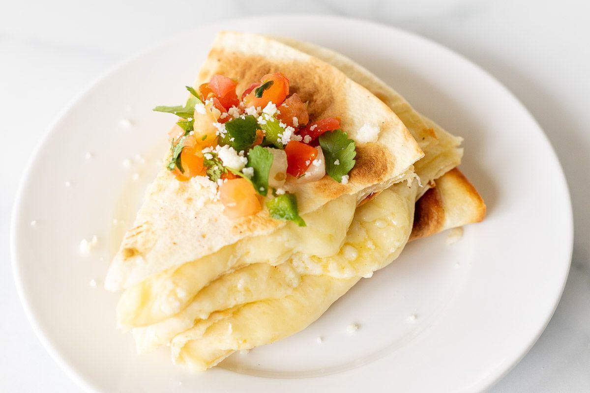 Käsequesadillas 7 In Scheiben geschnittene und gestapelte Käse-Quesadilla auf einem weißen Teller, mit Pico de Gallo belegt