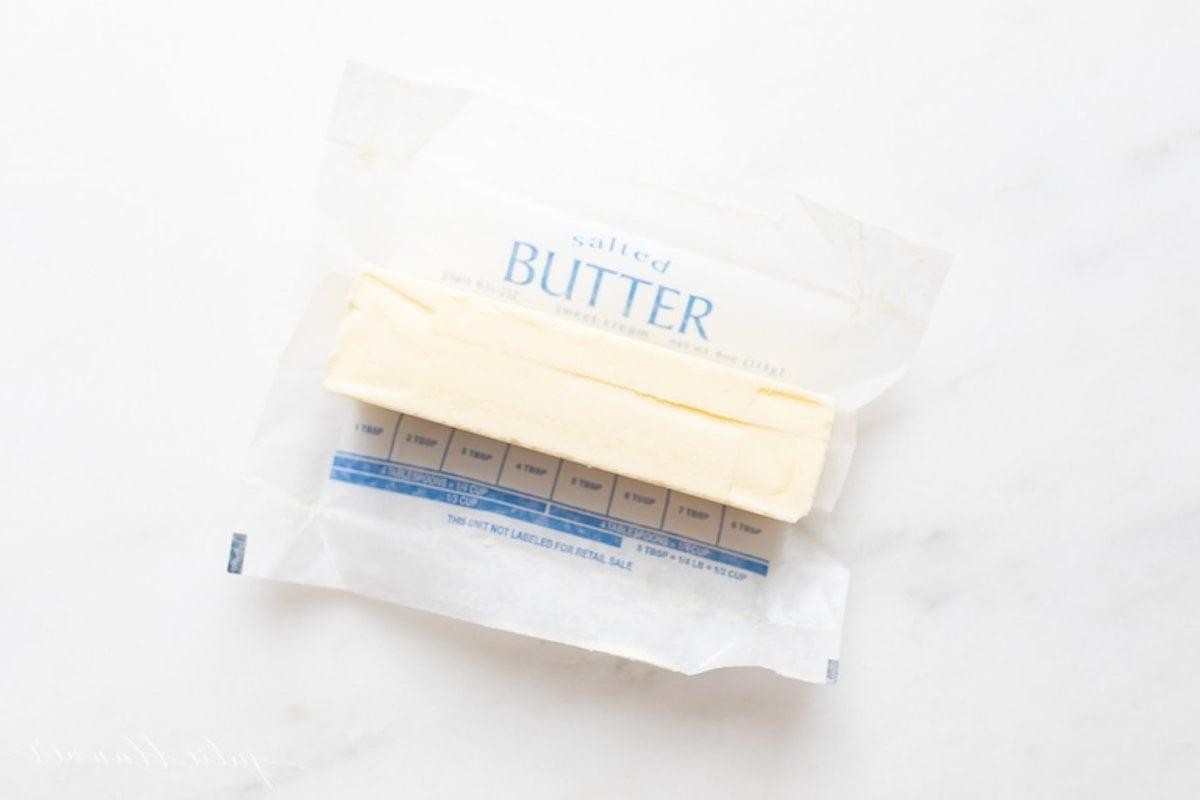 Ein einzelnes Stück gesalzene Butter auf einer Marmorarbeitsplatte, Papier darum gewickelt.