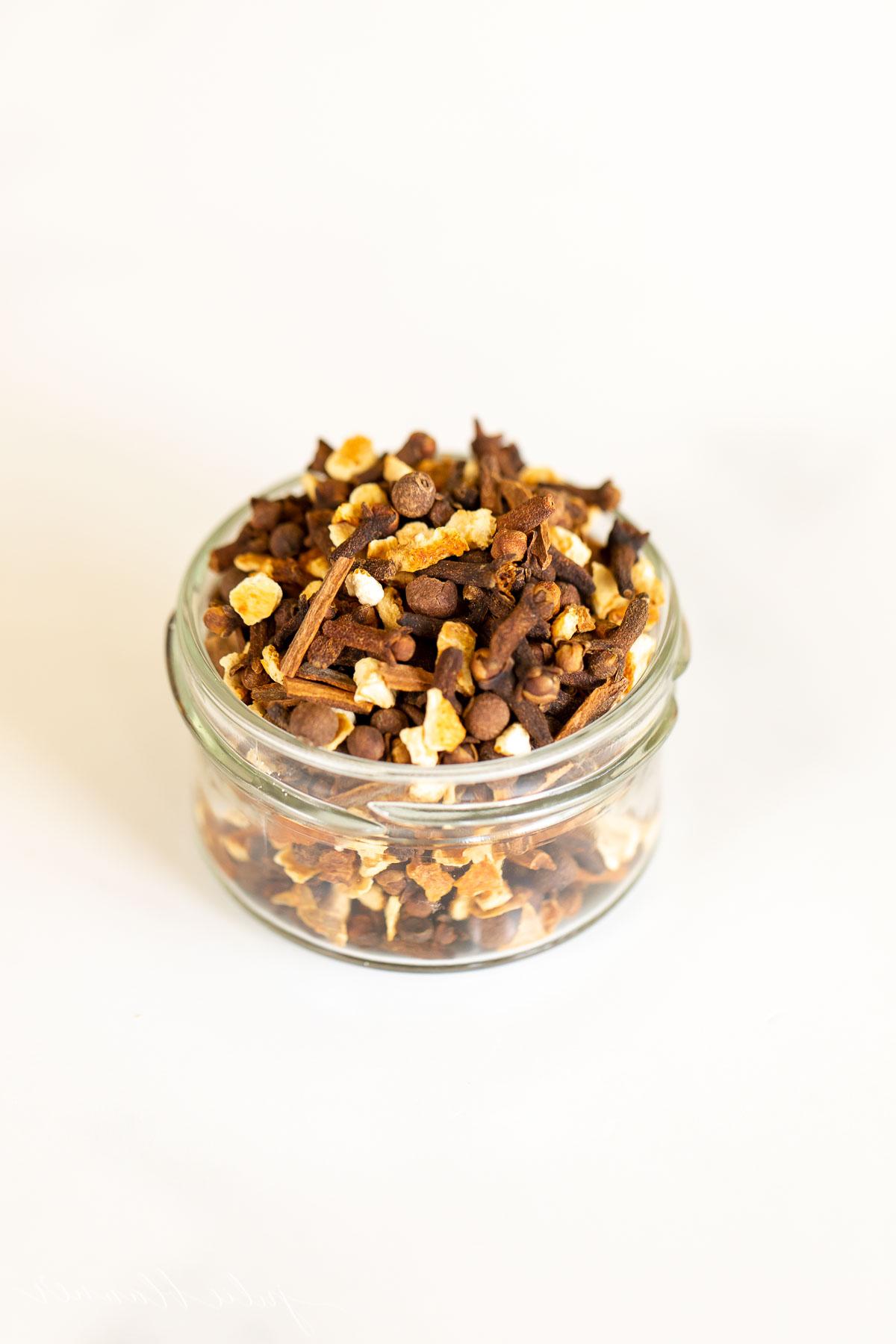 Glühweingewürze 5 Ein Glasgefäß gefüllt mit Zimt und anderen Gewürzen, die das Aroma von Glühweingewürz verströmen, auf einer Holzoberfläche.
