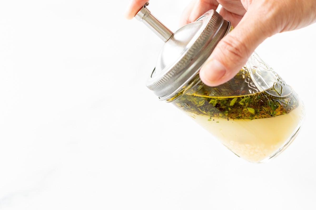Griechisches Hähnchen 7 Eine Hand hält ein Glasgefäß voller Marinade.