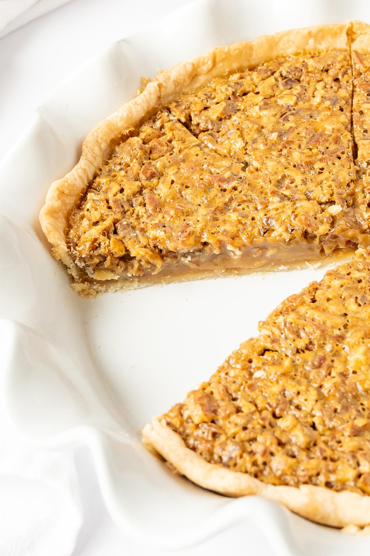 Ein köstlicher Karamell-Pekannusskuchen auf einem weißen Teller, aus dem ein Stück herausgeschnitten wurde. Ein perfektes Dessert für jeden Anlass.