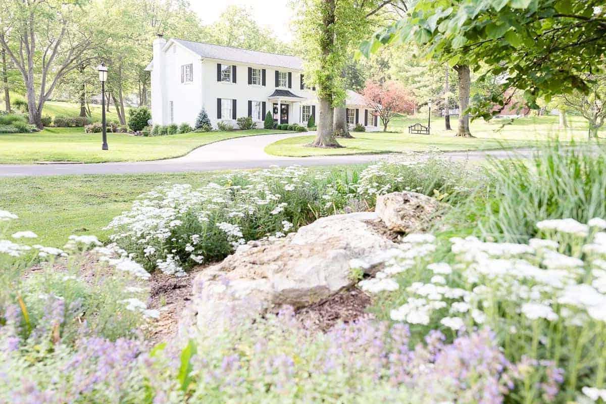 Benjamin Moore Einfach Weiß 7 Ein kolonialer Backsteinhaus, gestrichen in Benjamin Moore Simply White, Blumen im Vordergrund des Bildes.