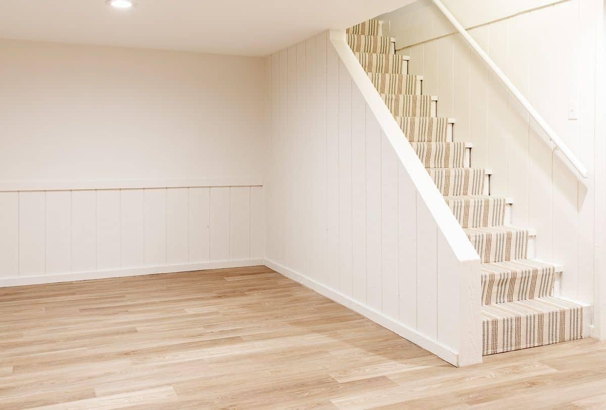 LVP-Vinyl-Dielenboden 7 Ein leerer Keller mit weißen Wänden und einem mittelbraunen Vinyl-Designboden.