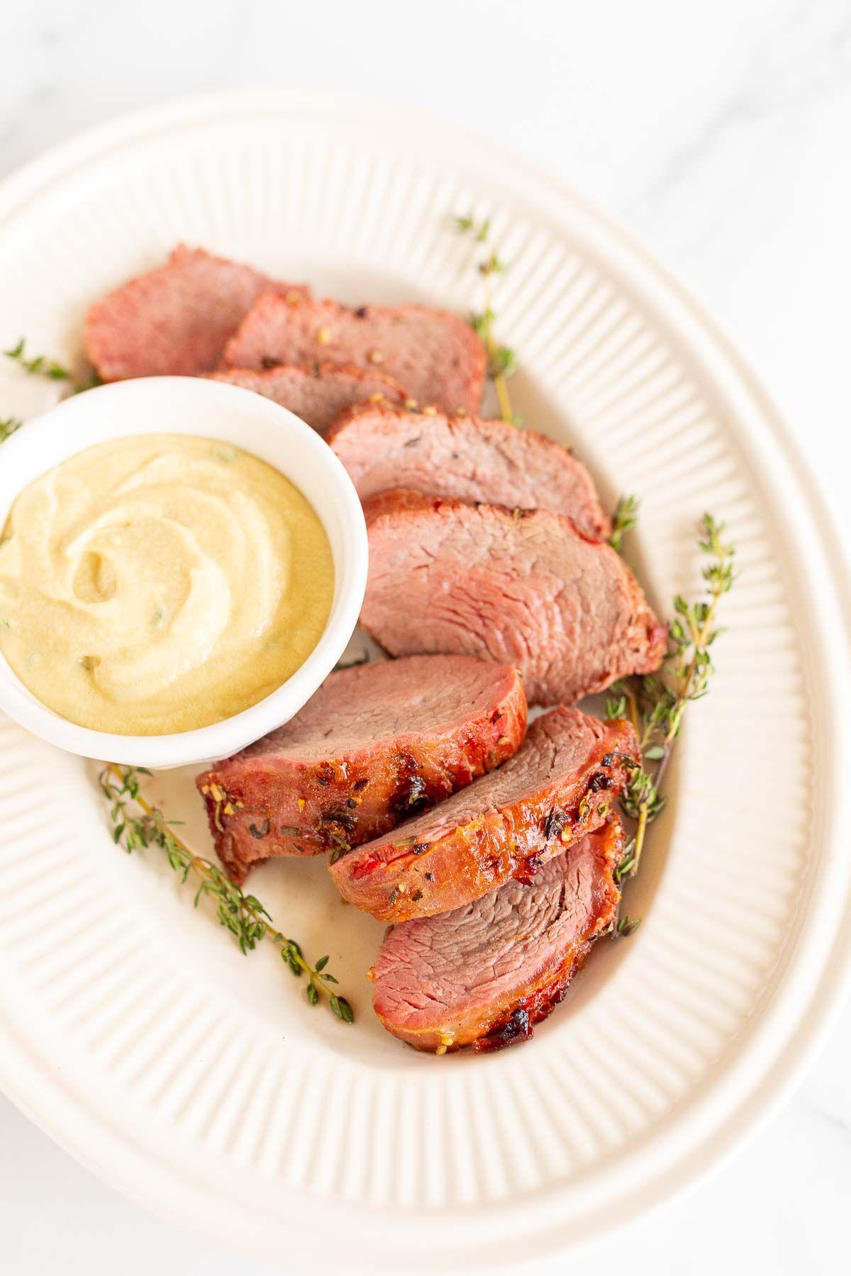 Eine weiße Schale voller Dijon-Senfsauce, umgeben von Rinderfilet auf einer Platte