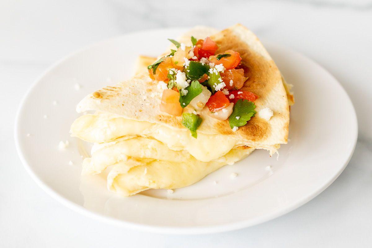 Käsequesadillas 8 In Scheiben geschnittene und gestapelte Käse-Quesadilla auf einem weißen Teller, mit Pico de Gallo belegt