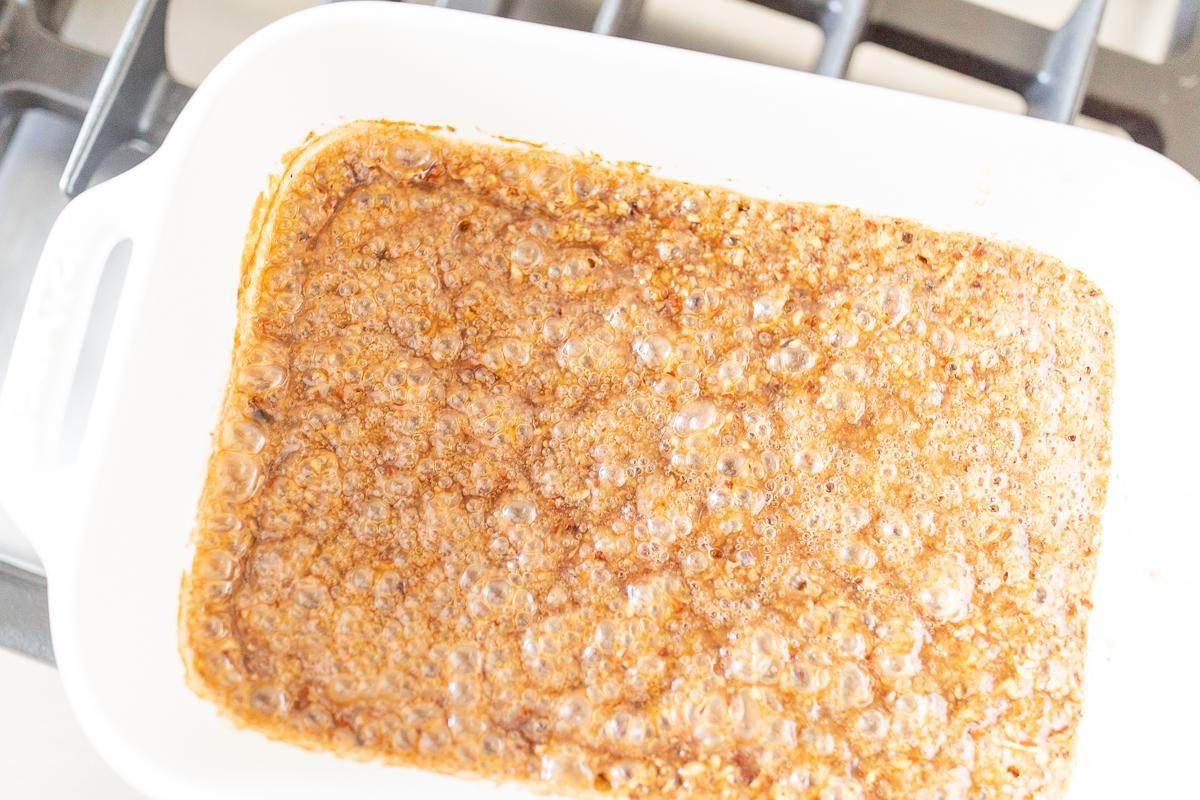 Eine quadratische Auflaufform mit Karamellsauce für Pekannuss-Sticky Rolls.