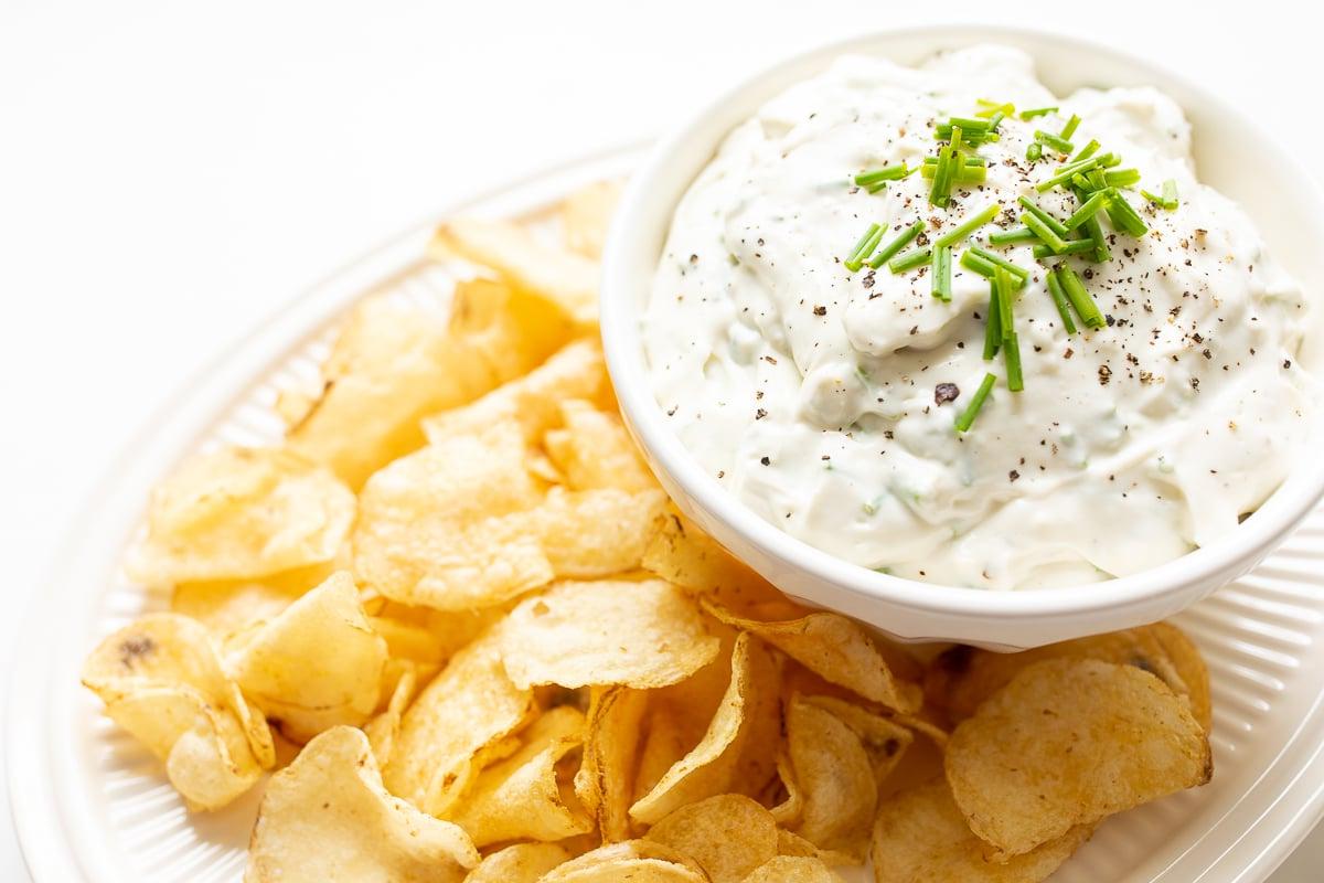 Ein Blauschimmelkäse-Dip in einer weißen Schale, appetitlich auf einer Servierplatte mit knusprigen Kartoffelchips angerichtet – ein perfekter Partysnack.