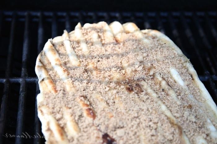 Pizzateig auf einem Außengrill ausgebreitet, belegt mit Zimt und braunem Zucker