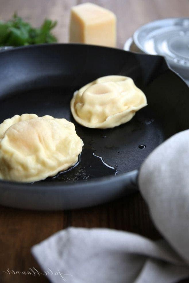 Hausgemachte Eier-Ravioli sind schnell und einfach zuzubereiten und eignen sich hervorragend als Vorspeise oder Hauptgericht. Ravioli gefüllt mit Käse und einem Eigelb, das einfach so beeindruckend ist. Die gekochten hausgemachten Eier-Ravioli in einer Gusseisenpfanne, bereit zum Servieren und Genießen.