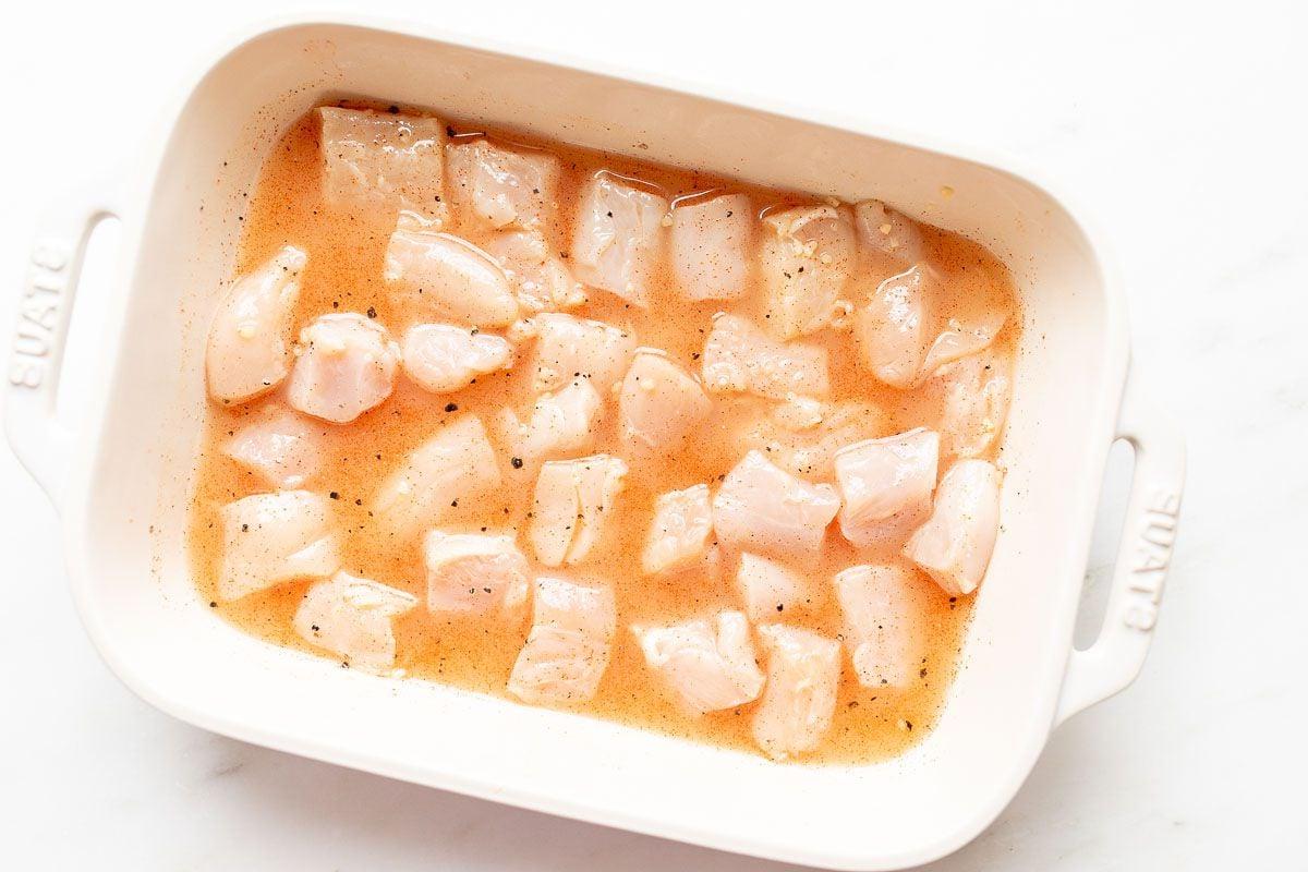 Hähnchenspieße-Marinade mit ungekochten Hähnchenstücken in einer weißen Auflaufform
