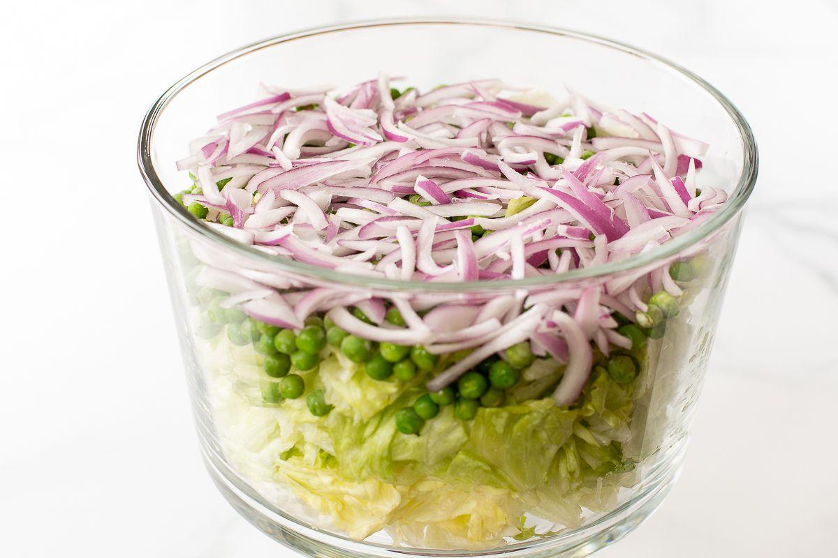 Gehackter Salat mit Erbsen und Zwiebeln in einer Glasschale.