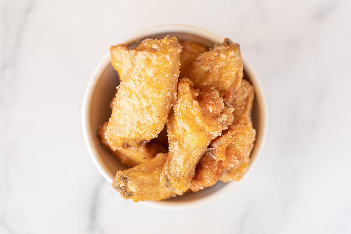 Knoblauch-Parmesan-Hähnchenflügel 9 Eine große, weiße Schale, prall gefüllt mit appetitlichen Knoblauch-Parmesan-Hähnchenflügeln, präsentiert auf einer eleganten Marmorarbeitsplatte