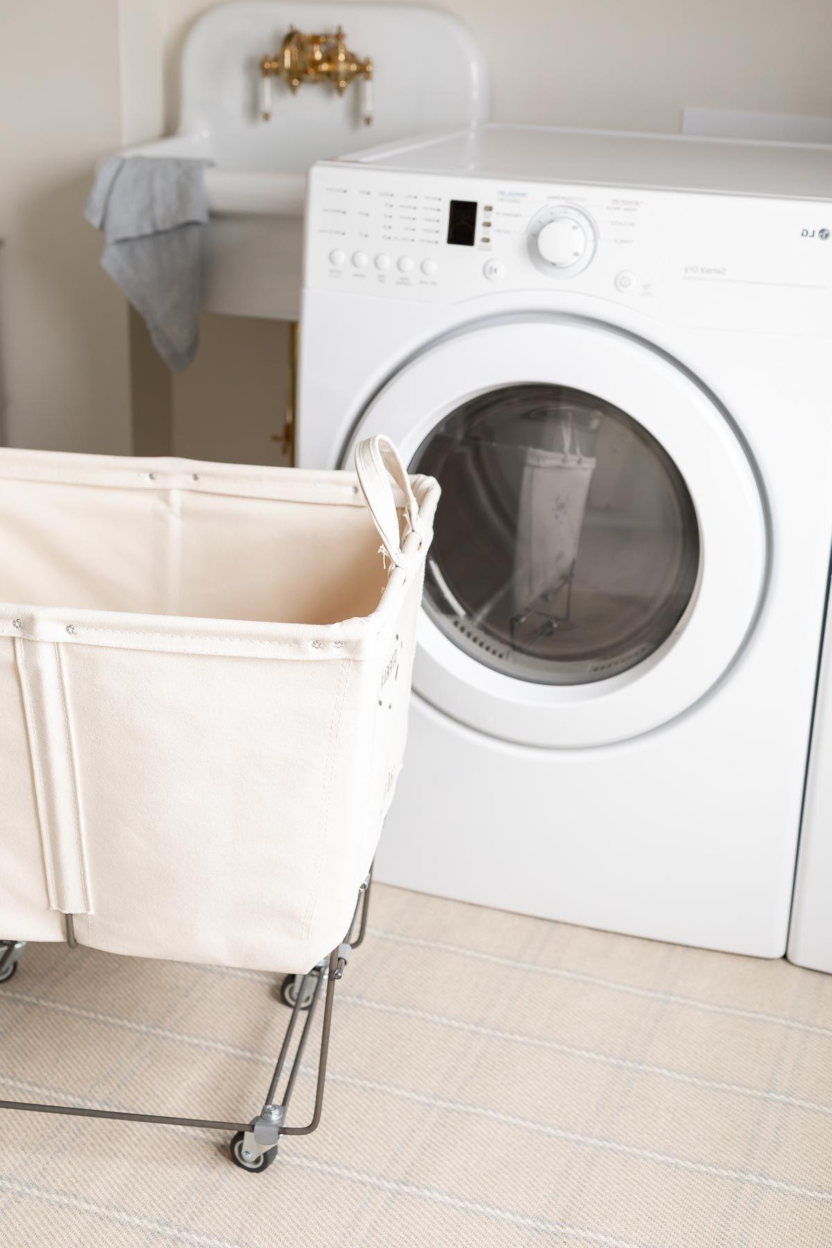 Teppiche auf Teppichboden schichten? 9 Eine Waschküche mit einem weißen Trockner, einem Vintage-Wäschekorb davor, platziert auf karierten Teppichen auf Teppichboden