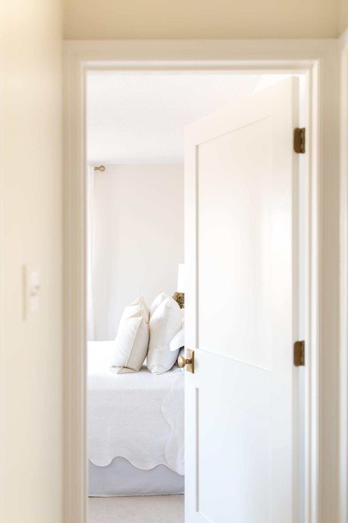 Innentüren streichen 9 Ein helles und luftiges Schlafzimmer, gesehen durch eine offene Tür, mit einem Gemälde an der Innenseite der Tür hängend.