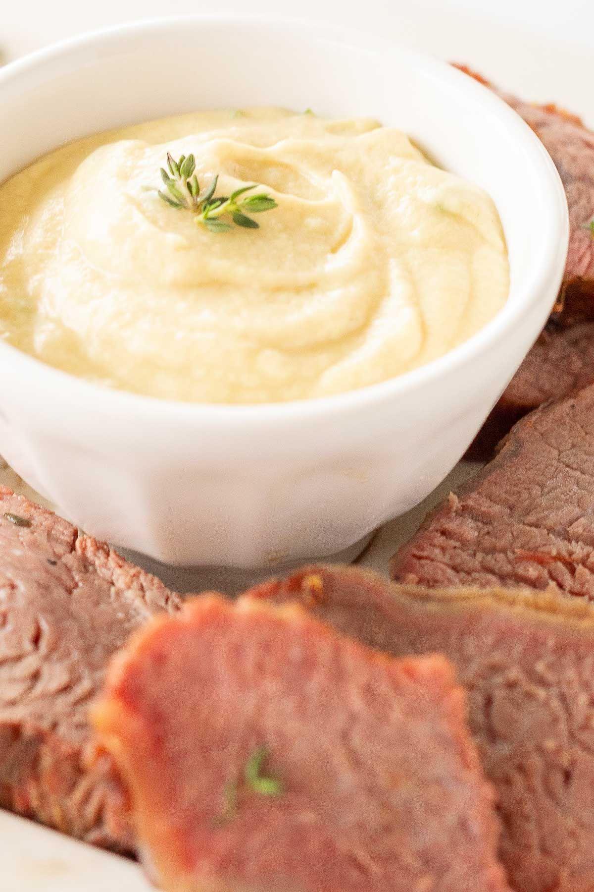 Eine weiße Schale voller Dijon-Sauce, umgeben von Rinderfilet.