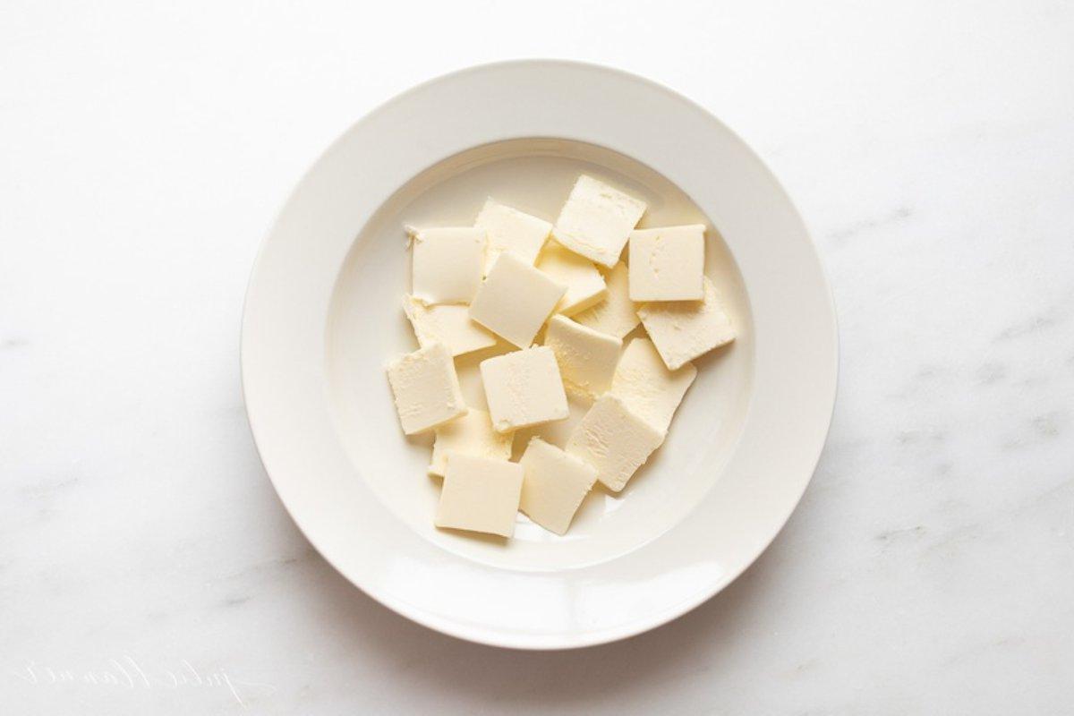Ein weißer Teller voller Butterstücke in einem Tutorial zum schnellen Weichmachen von Butter.