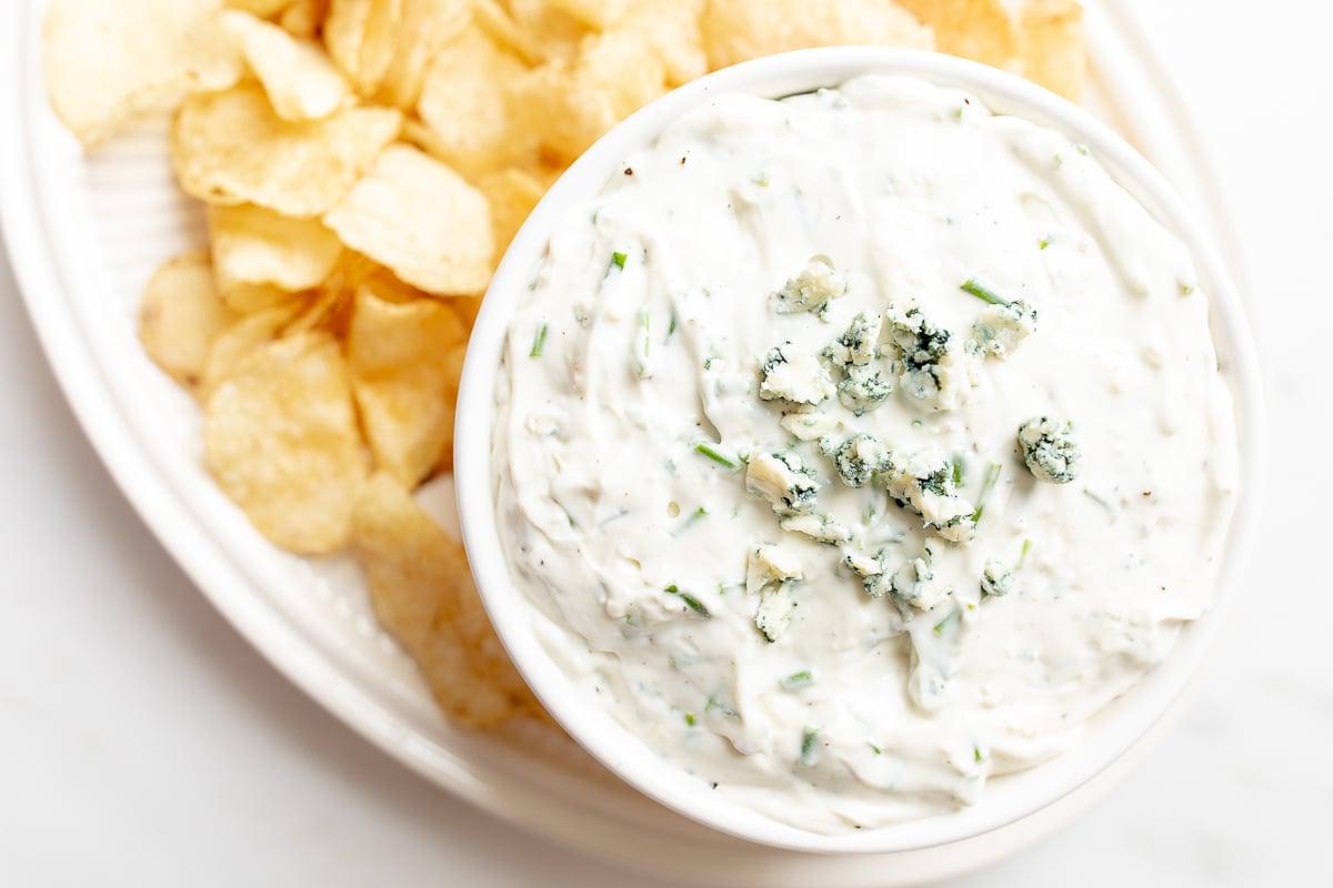 Ein appetitlich angerichteter Blauschimmelkäse-Dip in einer weißen Schale, umgeben von knusprigen Kartoffelchips auf einer Servierplatte.